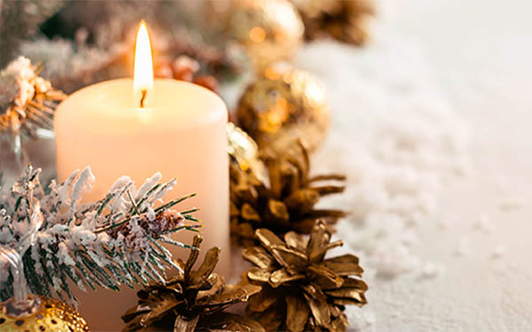 Burning white candle surrounded by winter greens, gold accents and snow