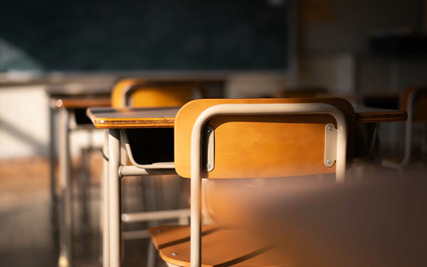 Empty school classroom with wooden chairs, desks, and a chalkboard.