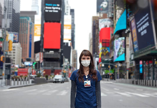 new york city healthcare worker standing in times square wearing hospital uniform and a mask