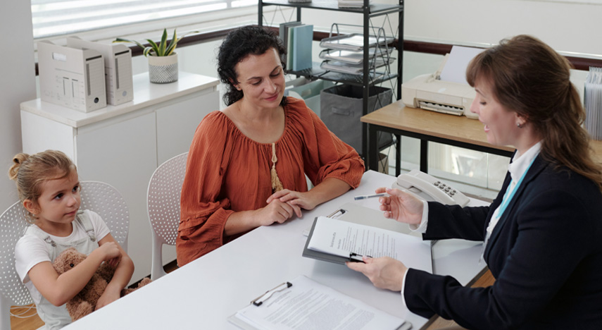 worker reviewing paperwork across desk with parent and child holding stuffed animal